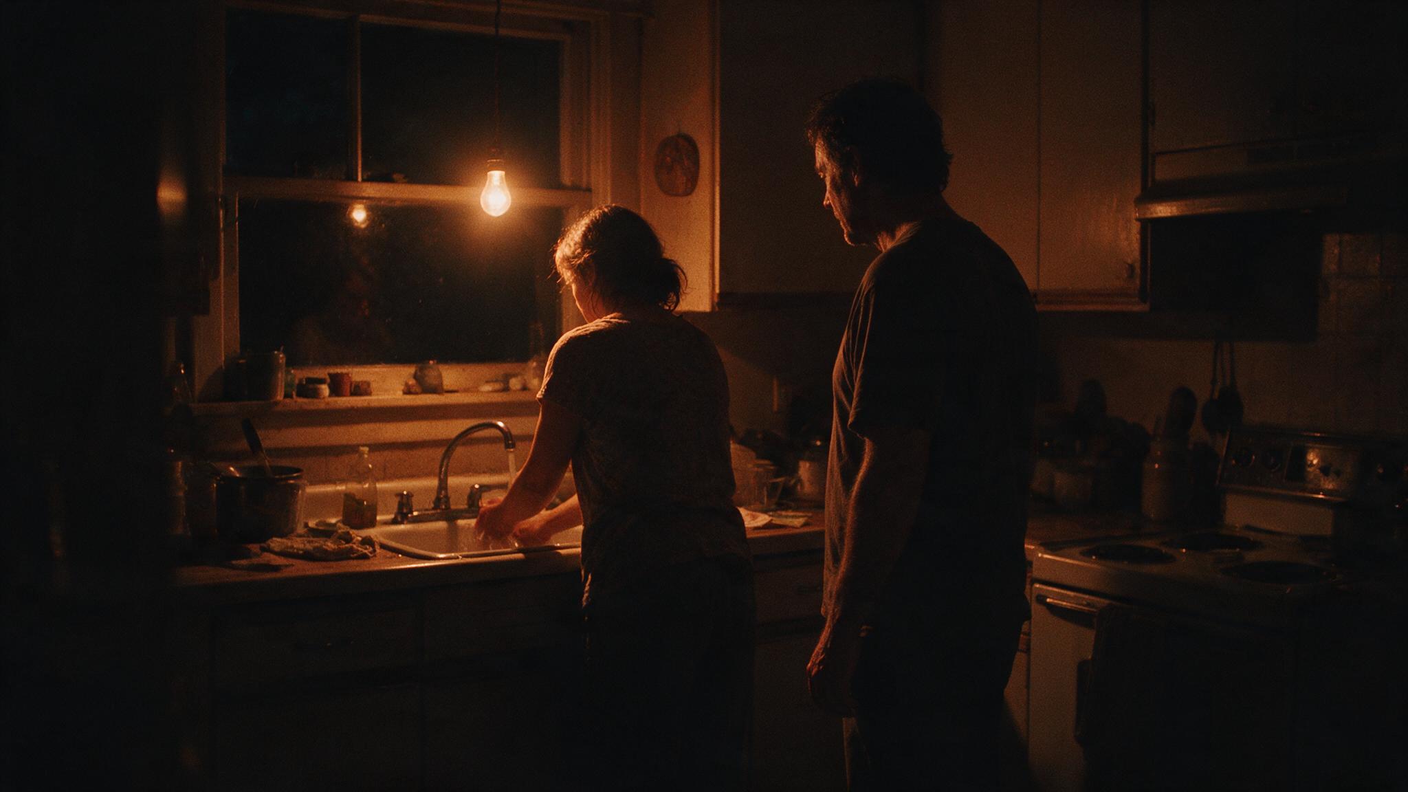A couple standing apart in a dim kitchen at night